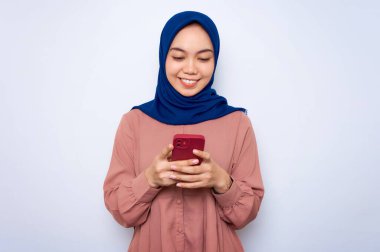 Smiling young Asian muslim woman in pink shirt using mobile phone and received good news isolated over white background. People religious lifestyle concept