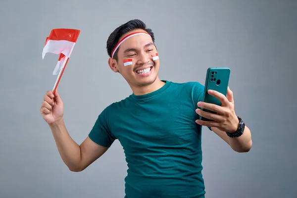 Excited Young Asian Man Holding Mobile Phone Indonesian Flag While — Stok fotoğraf