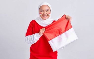 Smiling young Asian muslim woman in red white t-shirt celebrating indonesian independence day on 17 august with proudly to showing flag indonesian isolated on white background