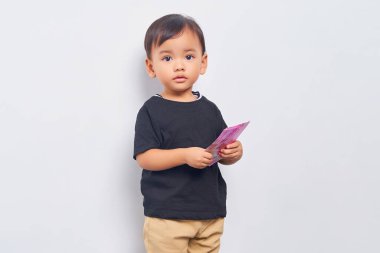 Smiling child kid boy 2 years wearing black t-shirt holding  Indonesian rupiah banknotes isolated on white background