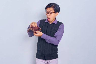 Beyaz arka planda izole edilmiş boş kahverengi cüzdana bakan şoke olmuş Asyalı genç bir adamın portresi.