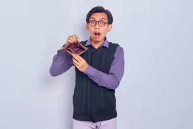 Beyaz arka planda boş kahverengi cüzdan gösteren şaşkın Asyalı genç bir adamın portresi.