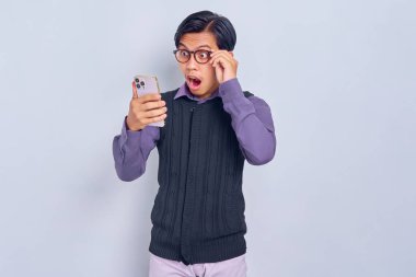 Sıradan gömlekli ve yelekli genç Asyalı şok olmuş, cep telefonu kullanmış, beyaz arka planda izole edilmiş gözlükleri çıkarmış. Halk yaşam tarzı konsepti