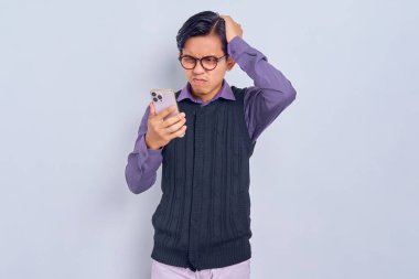 Kafası karışmış genç Asyalı bir adam beyaz arka planda akıllı telefonu kapalı tutarken kafasına dokunuyor. Halk yaşam tarzı konsepti