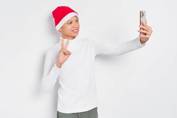 티셔츠를 산타클로스 모자를 잘생긴 아시아 배경에 고립된 휴대폰으로 셀피를 복용하고 — 스톡 사진