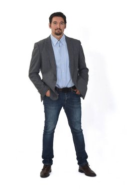 Ceketli, kot pantolonlu, elleri cebinde beyaz arka planda bir adamın ön görüntüsü.