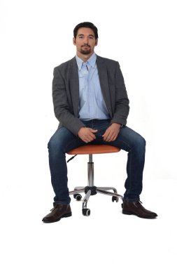 Sandalyeye oturmuş beyaz arka plandaki kameraya bakan bir adamın ön görüntüsü.