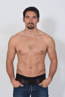 Bir adamın portriatı üstsüz, ciddi ve elleri beyaz arka planda.