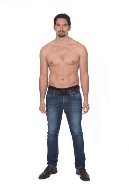 Üstsüz ve kot pantolonlu bir adam beyaz arka plandaki kameraya bakıyor.