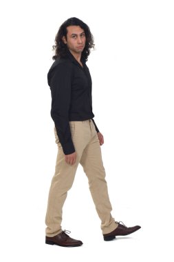 Uzun saçlı bir adamın beyaz arka planda yürümesi ve bakması.