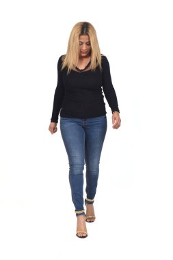 Kadın beyaz arka planda kot pantolon ve topuklu ayakkabılarla yürürken aşağıya bakıyor.