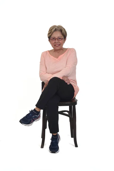 フロントビューの幸せなシニア女性の完全な肖像画の椅子に座っているスポーツウェアの足に身を包んだ白い背景に交差 — ストック写真