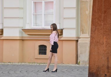 TIMISOARA, ROMANIA - 18 Nisan 2018: Güzel genç bir kadın sokakta fotoğraf çekimi yapıyor. Manken pembe bir bluz, kısa siyah bir etek, külotlu çorap ve yüksek topuklu ayakkabı giyiyor.