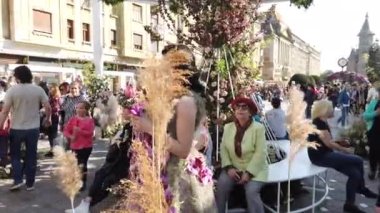 TIMISOARA, ROMANIA - 19 Nisan 2019: Zafer Meydanı, TIMFLORALIS Uluslararası Çiçek Festivali. Festivalin kraliçesi çiçekli bir elbise giyerek sokakta yürüyor..