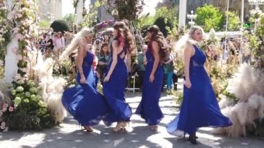 TIMISOARA, ROMANIA - 20 Nisan 2019: TIMFLORALIS Uluslararası Çiçek Festivali. Uzun mavi elbiseli kadın şehir merkezindeki çiçek süslemelerinin tadını çıkarıyor. Yavaş çekim görüntüleri