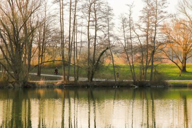Regensburg, Almanya - 25 Mart 2022: İnsanlar gün batımında Tuna Nehri boyunca, Almanya, Regensburg, Avrupa 'da kırsal bir yolda bisiklete biniyorlar..