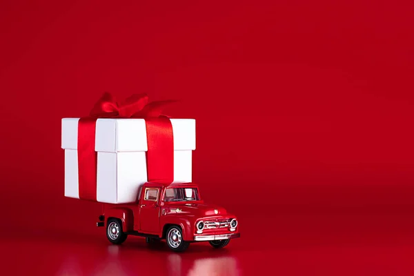 Red car with a gift box on a red background. Concept - delivery of gifts for the holidays, Valentines Day, International Womens Day, February 14, March 8. Shopping, sale — Fotografia de Stock