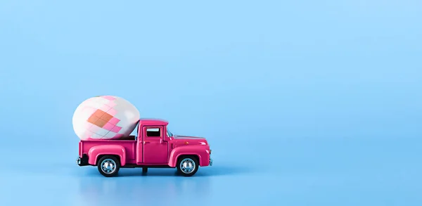 파란 배경에 있는 분홍 자동차 뒤에 부활절 달걀 이 있는 모습. 스톡 사진