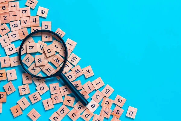 Kare ahşap karolardan yapılmış İngiliz alfabesi mavi arkaplana saçılmış. Düşünce geliştirme konsepti, dil bilgisi.