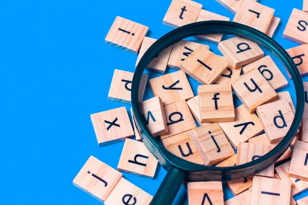 English alphabet made of square wooden tiles with the English alphabet scattered on blue background. The concept of thinking development,grammar.