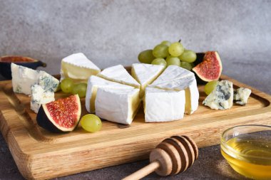 Camembert peyniri ve üzümlü mavi peynir tabağı, incir, tahta tahtada bal. Peynir tabağı