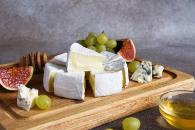 Camembert peyniri ve üzümlü mavi peynir tabağı, incir, tahta tahtada bal. Peynir tabağı