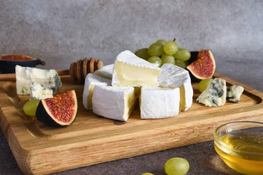 Camembert peyniri ve üzümlü mavi peynir tabağı, incir, tahta tahtada bal. Peynir tabağı