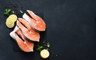 Siyah arka planda baharat ve klematisi olan çiğ kırmızı balık. Üst Manzara. Somon bifteği.