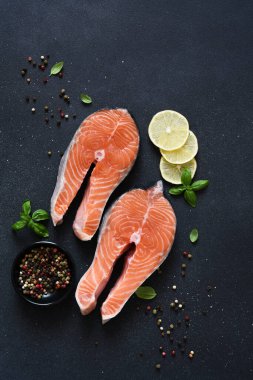 Siyah arka planda baharat ve klematisi olan çiğ kırmızı balık. Üst Manzara. Somon bifteği.