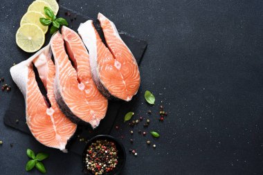 Siyah arka planda baharat ve klematisi olan çiğ kırmızı balık. Üst Manzara. Somon bifteği.