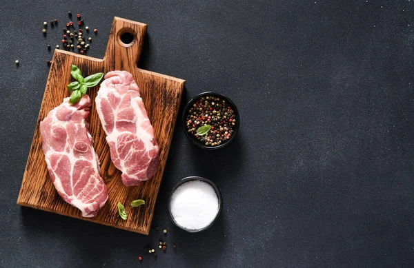 Baharatlı siyah arka planda ahşap bir tahtada domuz bifteği. Taze çiğ et..