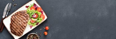 Salata ve sebzeli bir tabakta ızgara biftek ve koyu bir arka plan. Akşam yemeği.