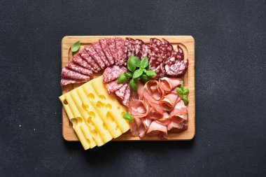 Peynir, prosciutto, siyah taşlı arka planda tahta bir tahta üzerinde salam. Hassasiyet.