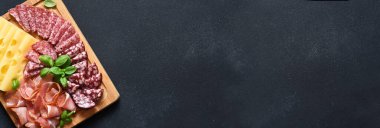 Peynir, prosciutto, siyah taşlı arka planda tahta bir tahta üzerinde salam. Hassasiyet.
