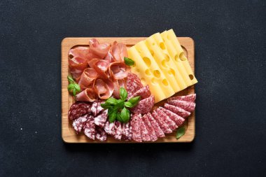 Peynir, prosciutto, siyah taşlı arka planda tahta bir tahta üzerinde salam. Hassasiyet.