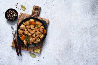 Baharatlı ve havuçlu güveç, dökme demir bir tavada güveç beton bir arka planda domatesli.