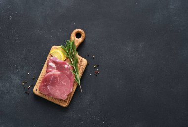 Tahtada taze çiğ et, siyah arka planda biberiye ve limon, domuz eti.