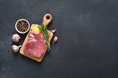 Tahtada taze çiğ et, siyah arka planda biberiye ve limon, domuz eti.