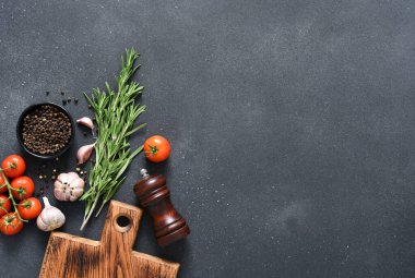 Siyah beton arka planda baharatlar. Ahşap tahta, biberiye ve domatesler mutfak masasında..
