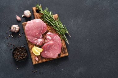 Tahtada taze çiğ et, siyah arka planda biberiye ve limon, domuz eti.