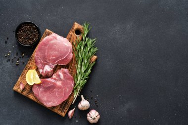 Tahtada taze çiğ et, siyah arka planda biberiye ve limon, domuz bifteği.