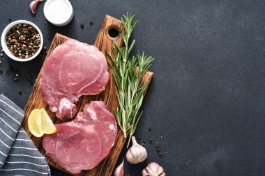 Tahtada taze çiğ et, siyah arka planda biberiye ve limon, domuz bifteği.