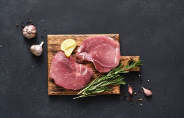 Tahtada taze çiğ et, siyah arka planda biberiye ve limon, domuz bifteği.