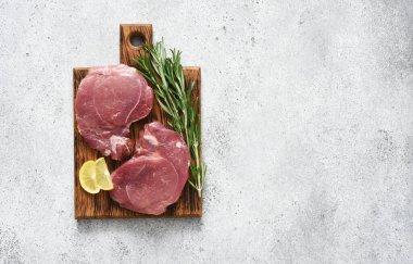 Hafif beton arka planda taze domuz bifteği, mutfak masasında baharatlı çiğ et, üst manzara.