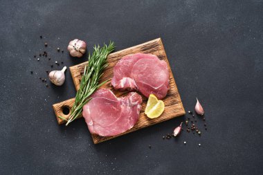 Tahtada taze çiğ et, siyah arka planda biberiye ve limon, domuz bifteği.