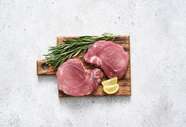 Hafif beton arka planda taze domuz bifteği, mutfak masasında baharatlı çiğ et, üst manzara.
