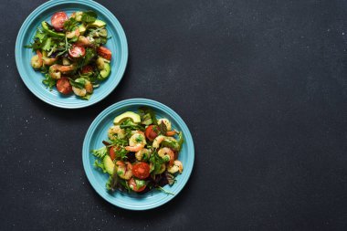 Salatayı domatesle karıştır ve karides ile pesto sosunu siyah bir zemine koy. Yukarıdan görüntüle