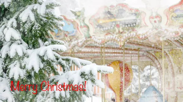 雪の中でカラフルなフランスのカルーセルを背景に雪の下でスプルースの枝のクローズアップ 自然の雪の冬の背景 ポストカード ポスター 碑文と招待状メリークリスマス — ストック写真