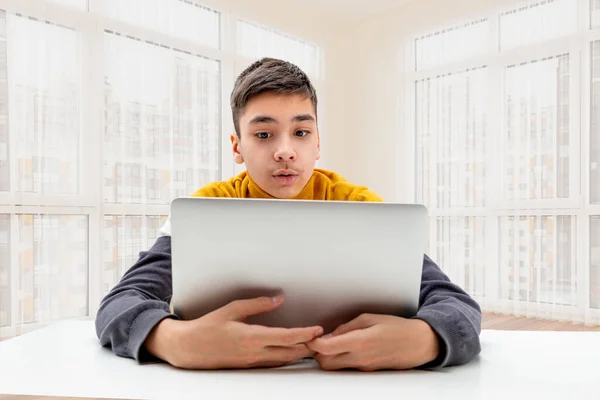 在房间里 一个穿着黄色衬衫的小男孩用笔记本电脑射击 他用你的胳膊环抱着笔记本电脑 — 图库照片