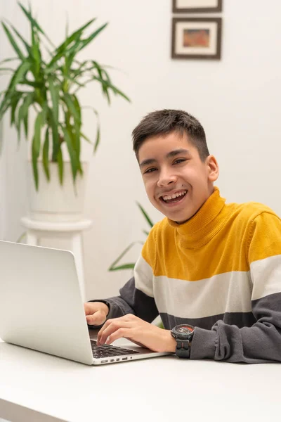 在房间里 一个身穿黄色衬衫 笑着的小男孩坐在桌子旁 手里拿着笔记本电脑 被枪击中 他在感情上玩电脑游戏或在网上交流 — 图库照片